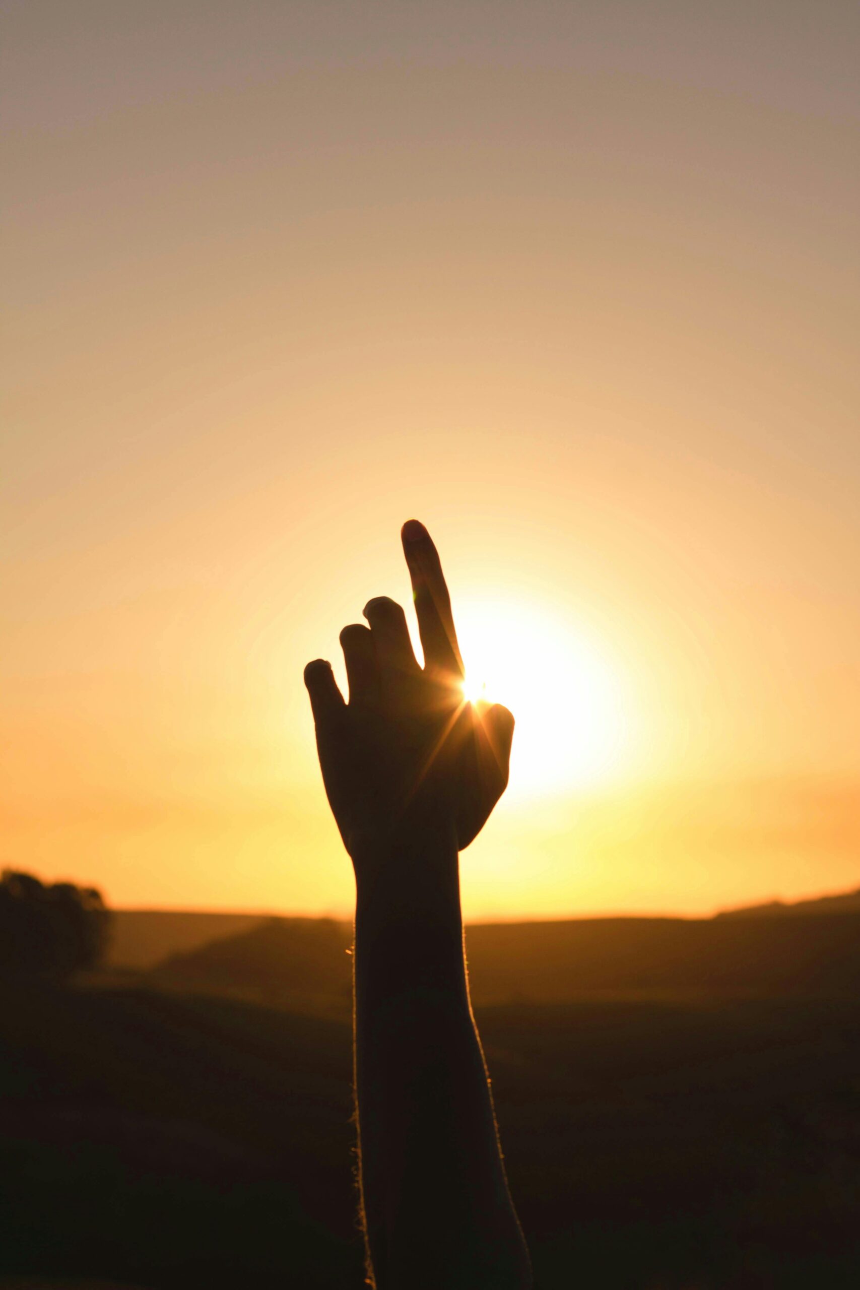 A silhouetted hand reaches towards the bright sun during a serene sunset, capturing the essence of golden hour.